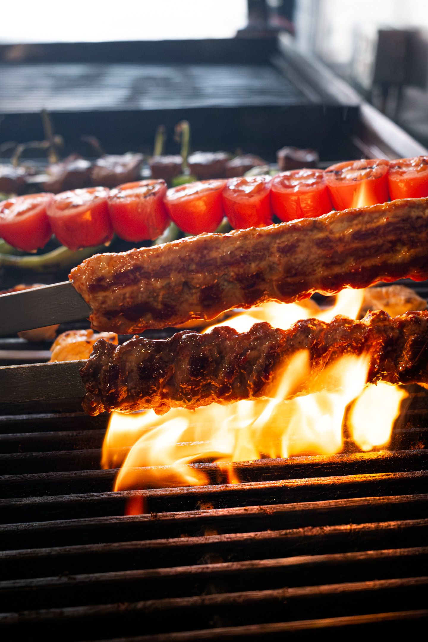 Restaurant photography of meat and vegetables cooking on a flaming grill with bright orange flames.