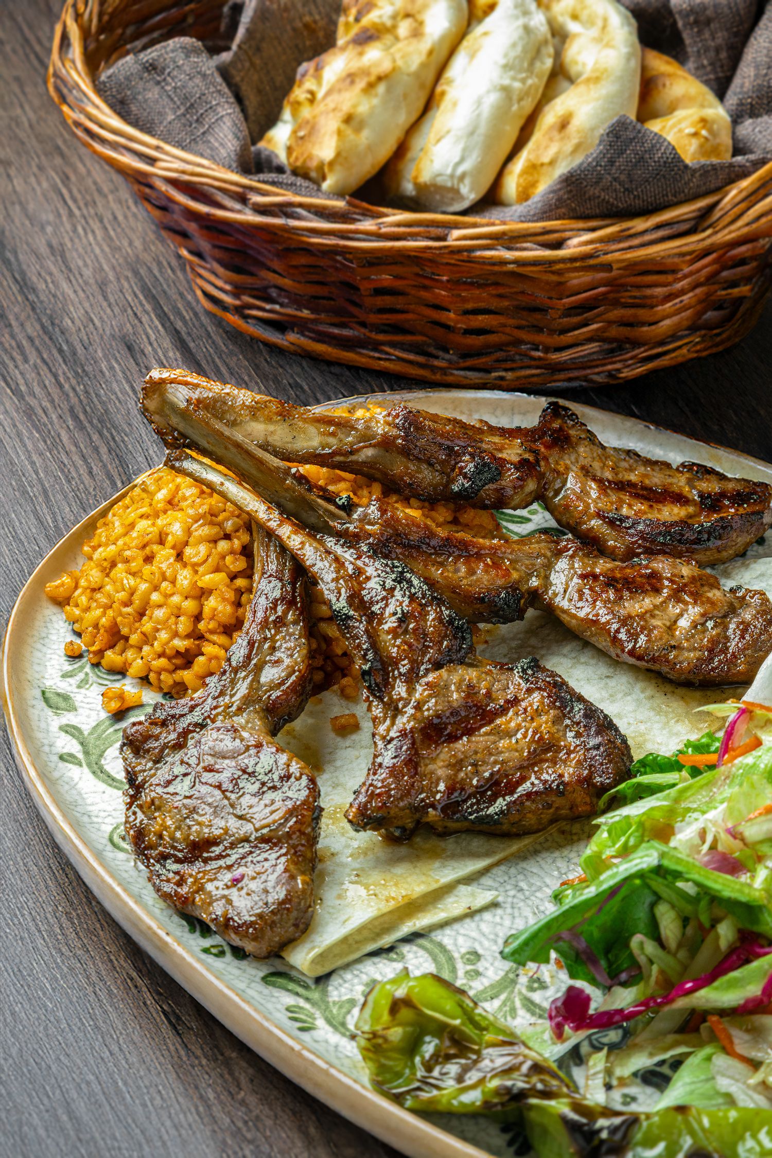 Grilled lamb chops served with mixed salad and corn on a decorative plate on dark wooden surface.