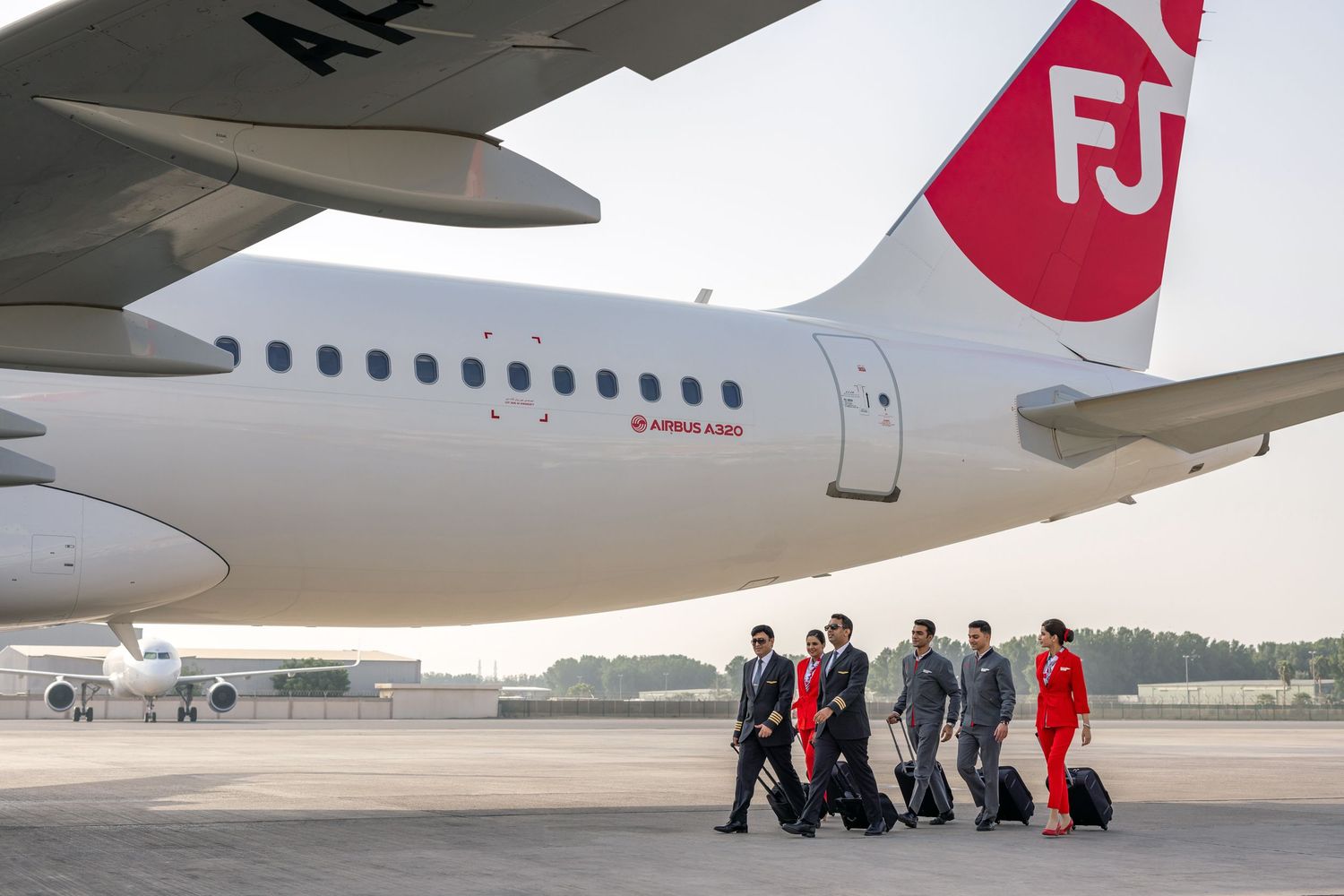 Airline crew walking on the tarmac with luggage beneath an FJ aircraft wing, shot for airline photography and video content.