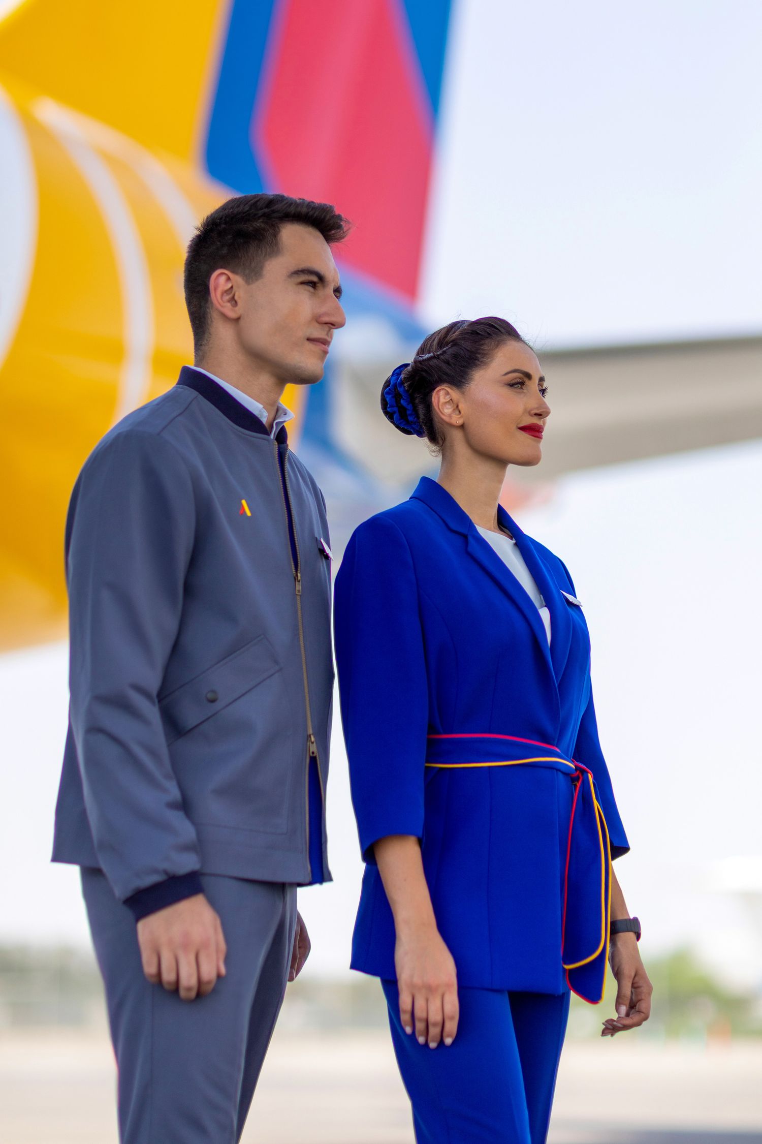 Airline crew in grey and blue uniforms standing beside a colorful aircraft tail, captured for branded airline content.