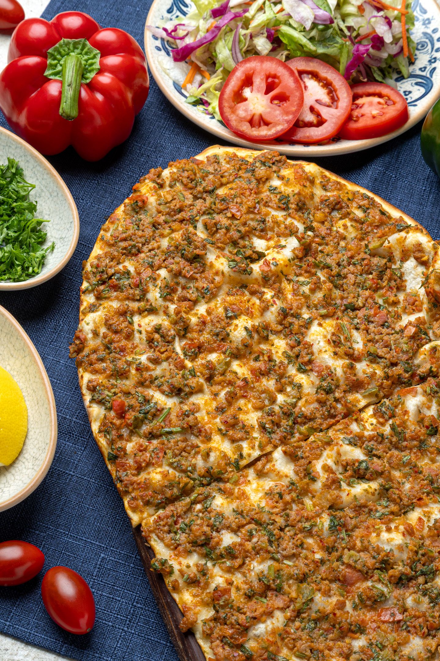 Menu photography of a Traditional Turkish lahmacun flatbread topped with spiced minced meat and fresh herbs.