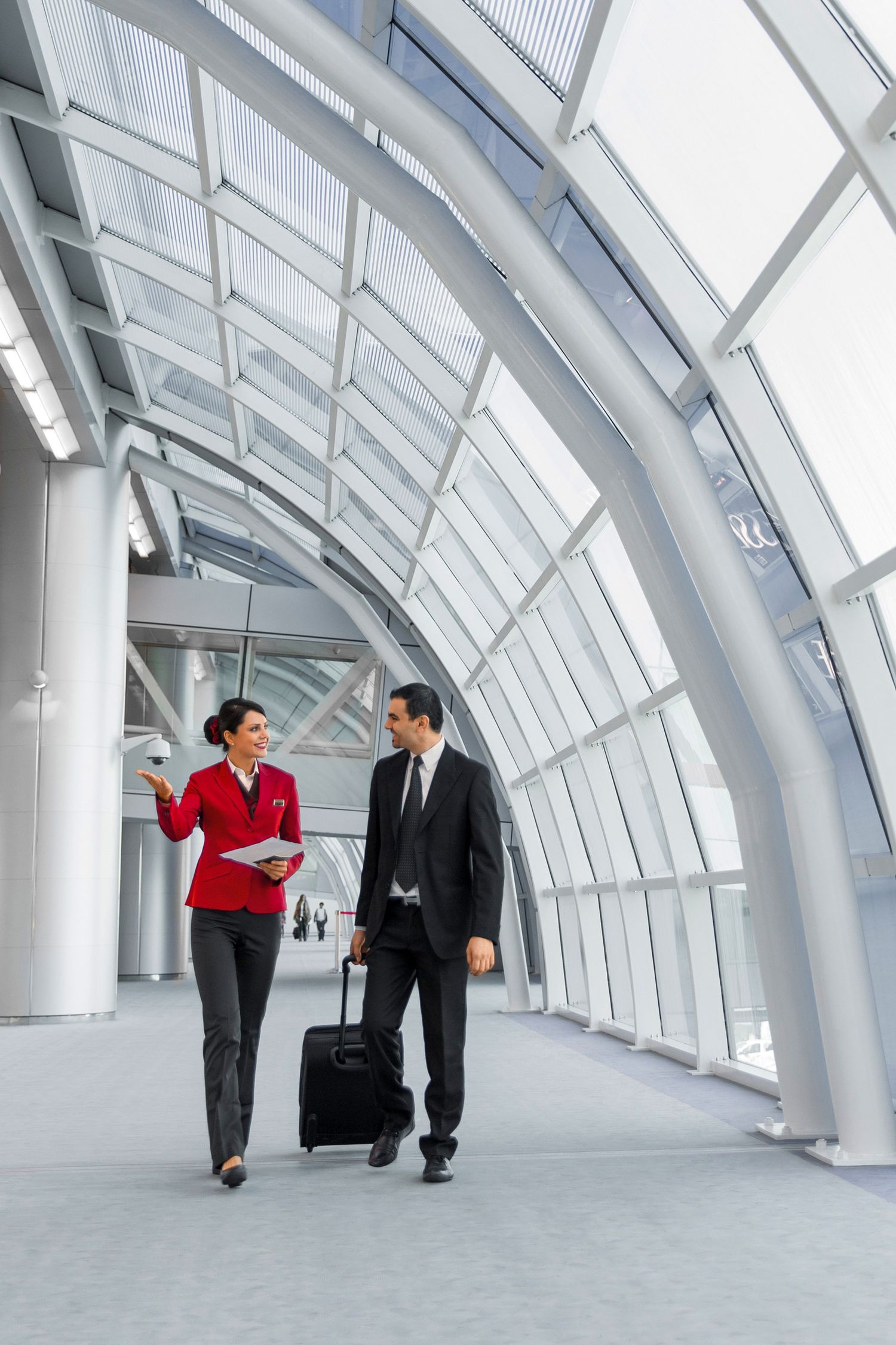 Business traveler with luggage walks alongside airline staff in a modern airport terminal corridor.