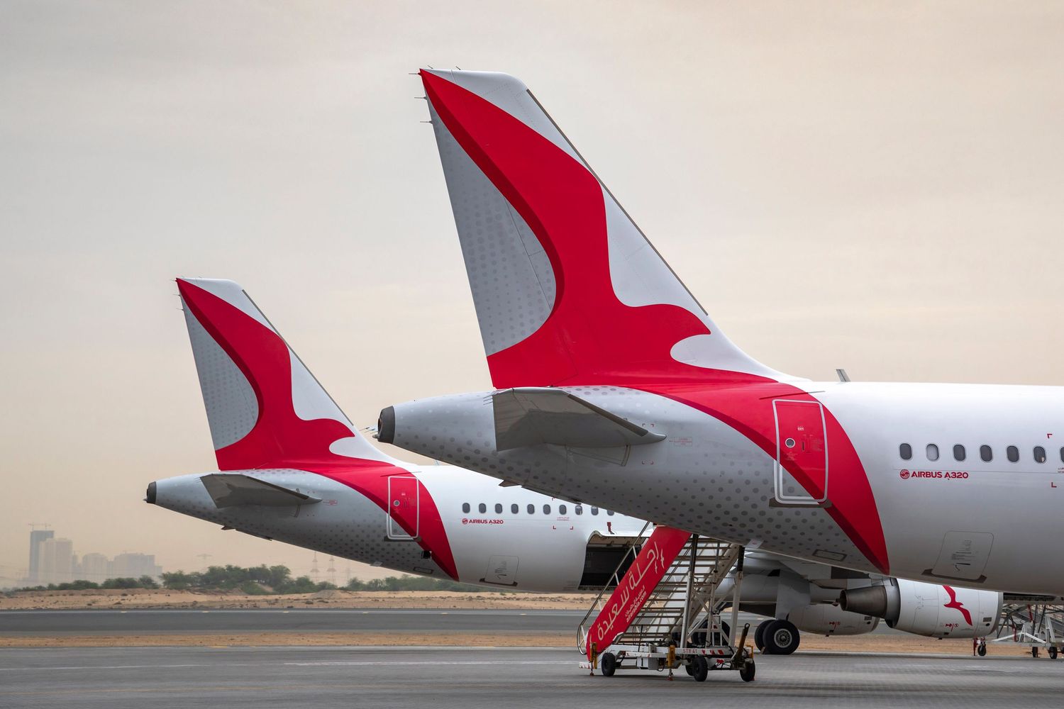 Airline aircraft tails visual content with red winglets lined up on the airport apron.