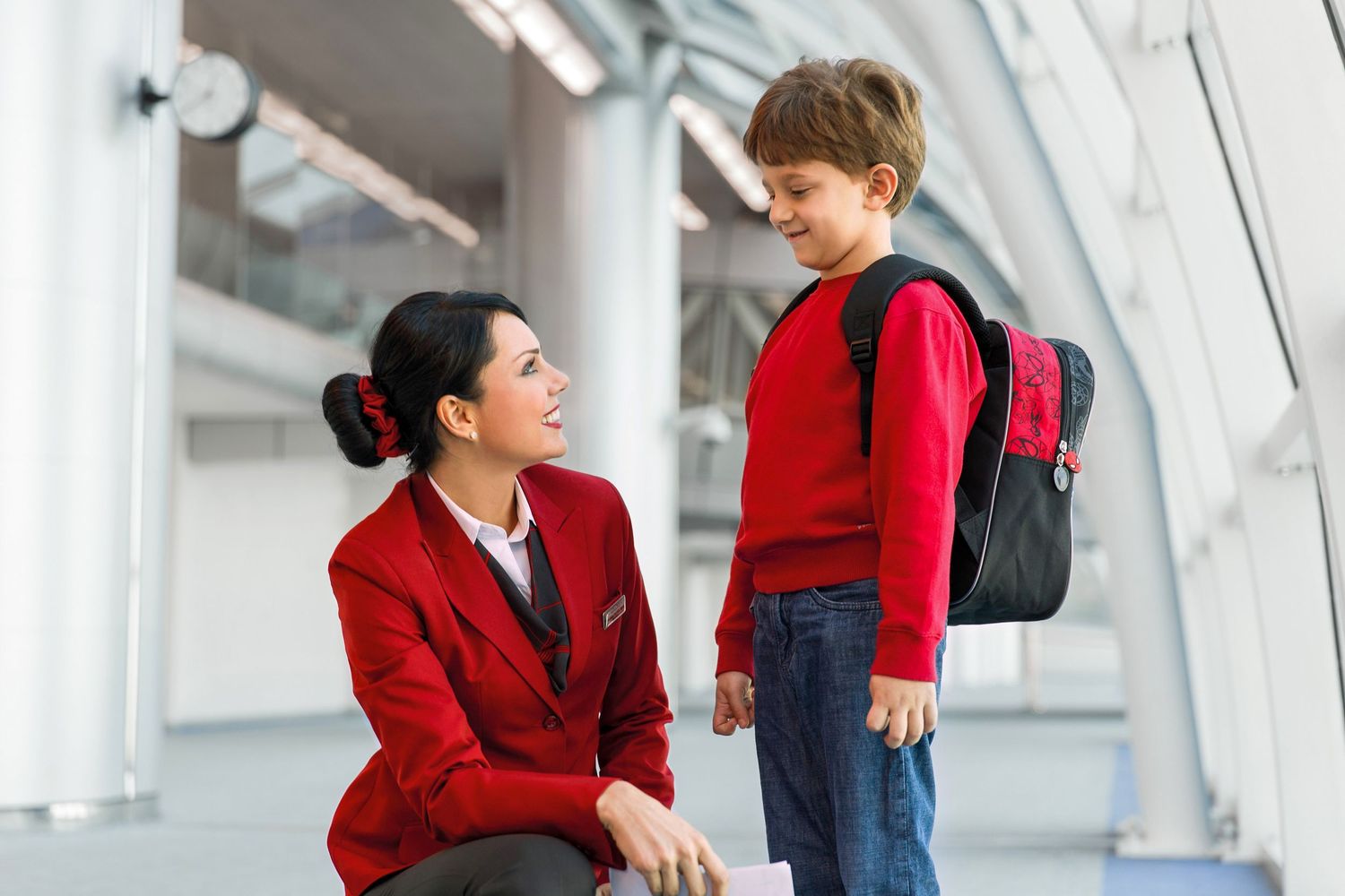 Airline crew member assists a young traveler with a backpack in a modern airport setting, captured for branded airline media.
