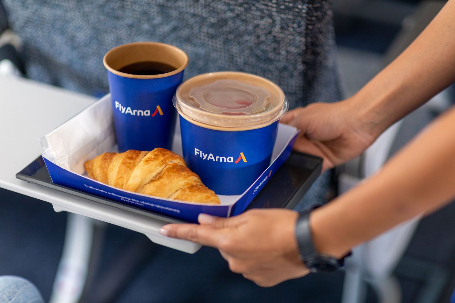 Inflight service photography with coffee and croissants served in blue branded cups by cabin crew