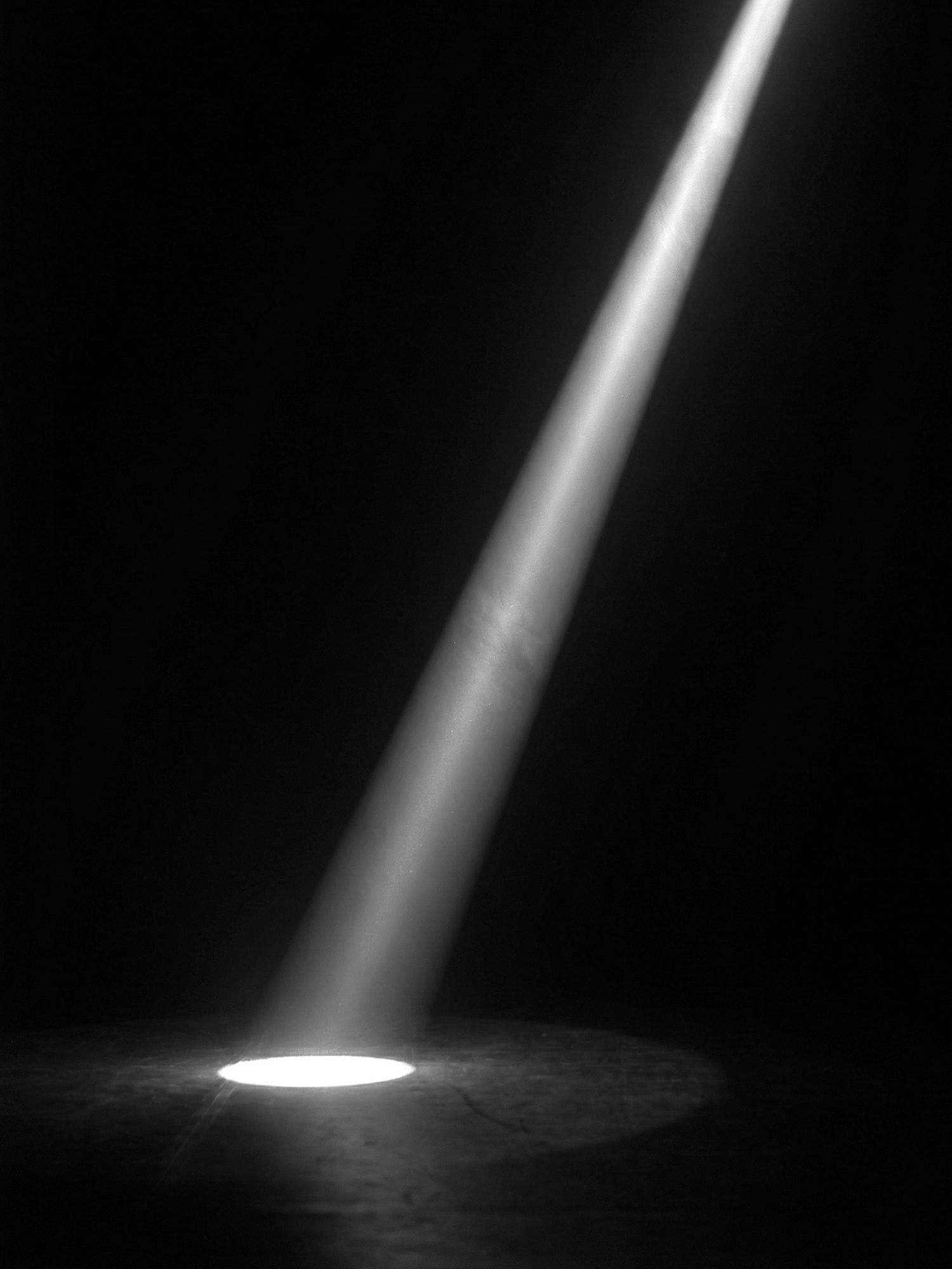 A dramatic beam of light shines down through darkness onto a reflective surface creating an ethereal spotlight effect.