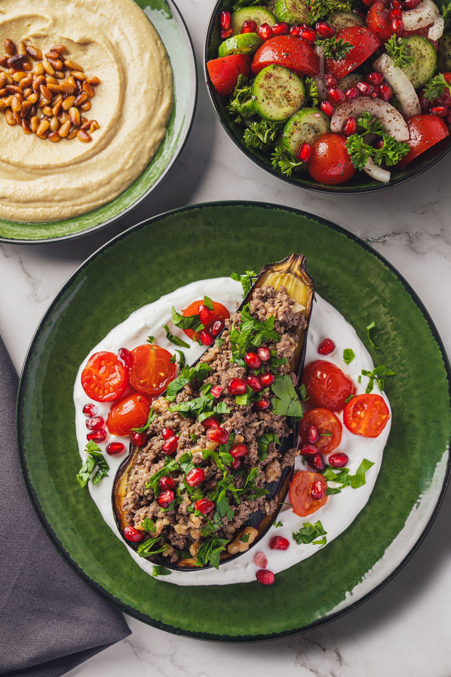 Stuffed eggplant with ground meat, pomegranate, tomatoes on yogurt sauce, served with hummus and fresh salad.