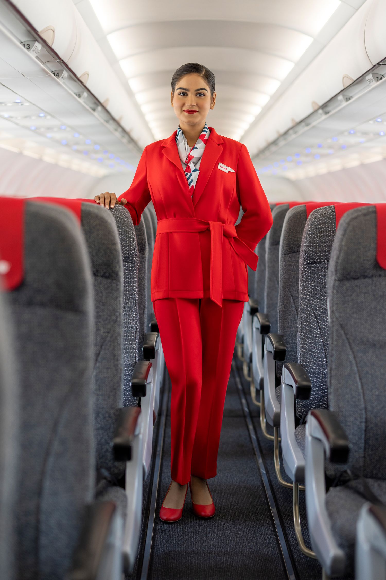 Flight attendant in a bold red uniform standing in the aircraft aisle, captured for branded airline photography and marketing.