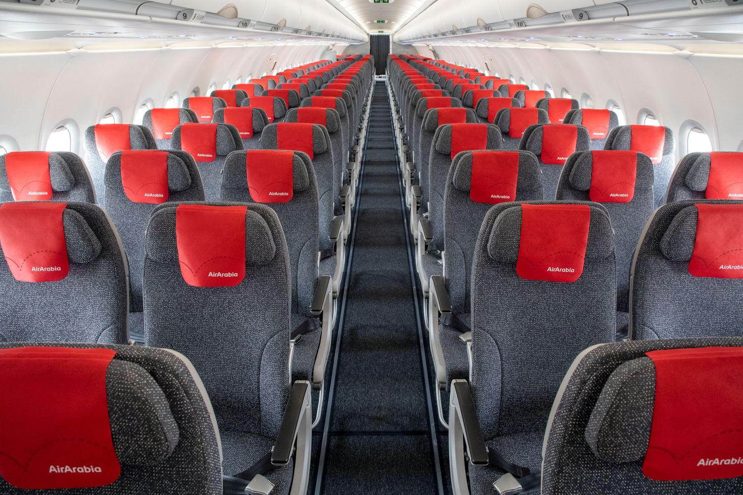 Airline cabin interior photography with red and gray passenger seats extending down the aisle.