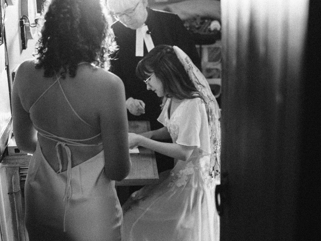 Black and white photo of a bride and flower girl in white dresses preparing together before a wedding ceremony.