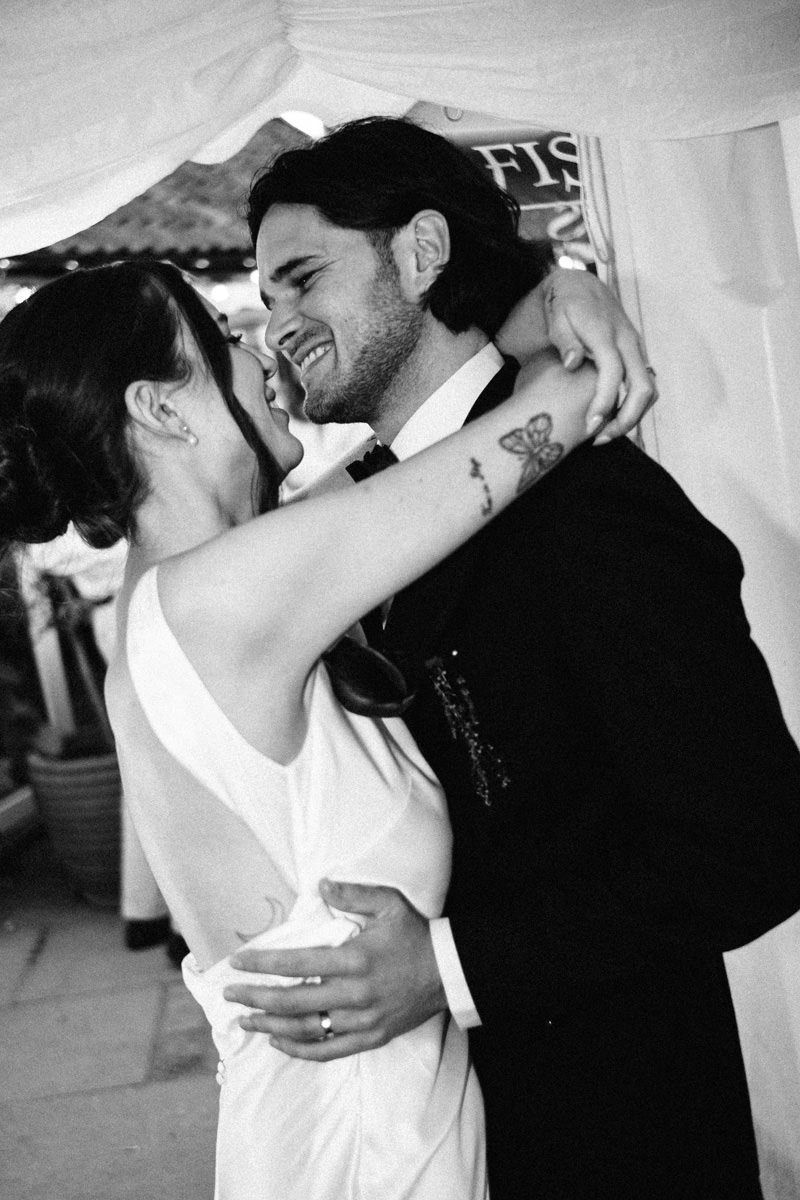 Black and white close-up of bride and groom sharing an intimate laughing embrace during first dance.