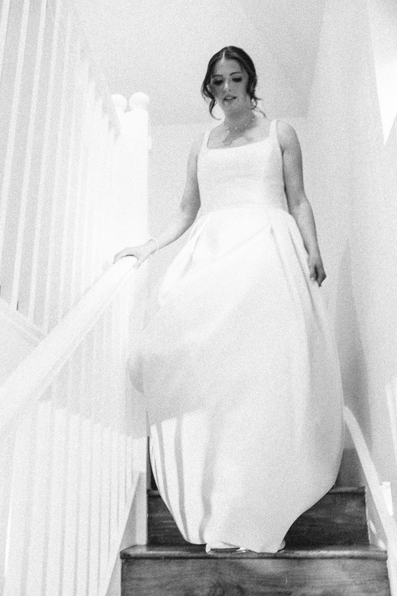 Elegant bride in ball gown wedding dress walking down stairs, black and white photo.
