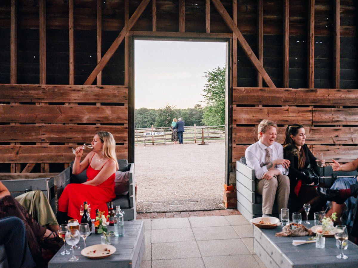 Wedding guests socializing inside rustic barn venue with open doors to countryside.