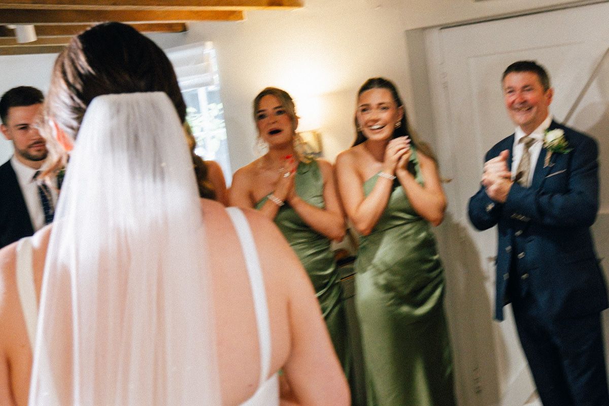 Bridesmaids in green satin dresses reacting emotionally during bride's first look reveal.