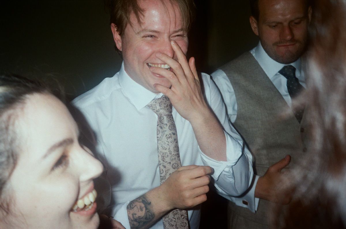 A man laughs joyfully surrounded by guests at a lively wedding celebration.