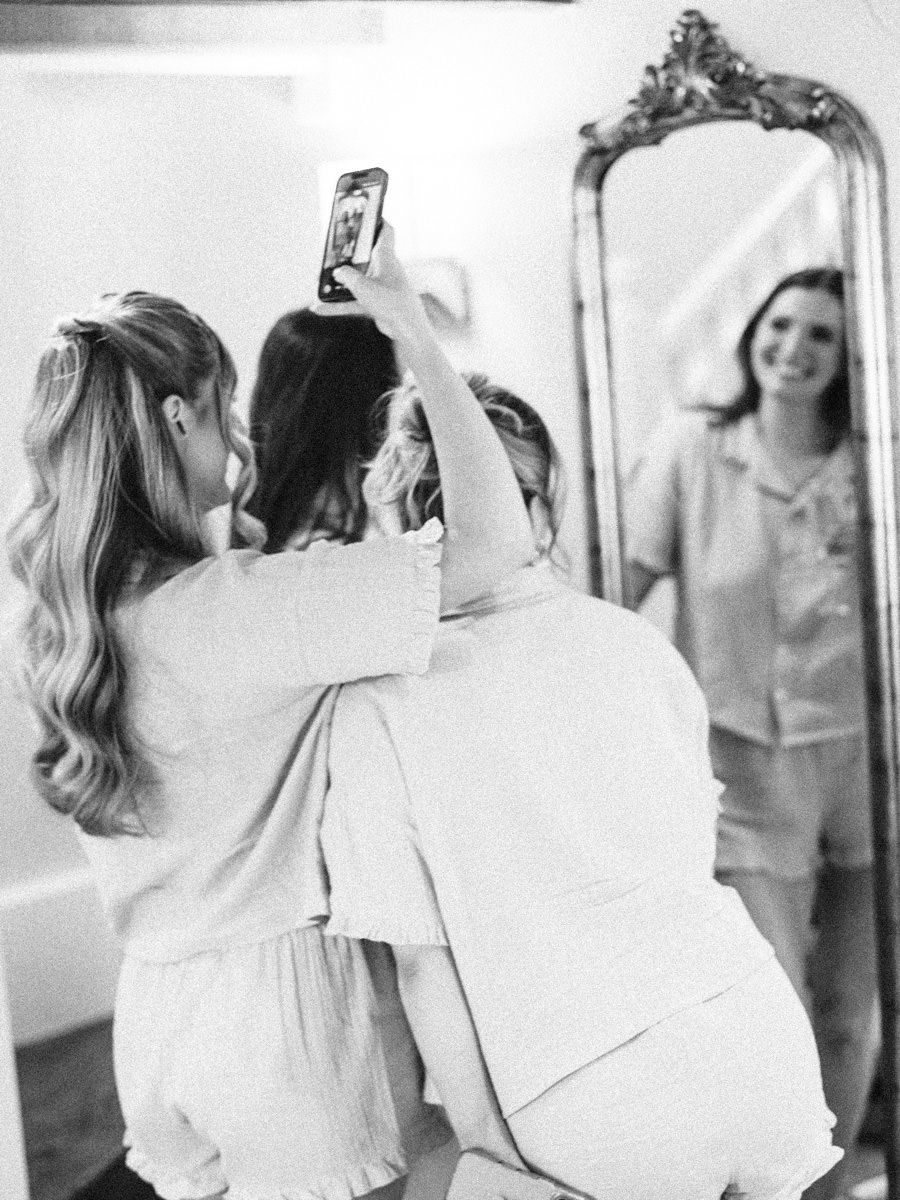 Bridesmaids taking a selfie together in front of an ornate gold mirror while getting ready.