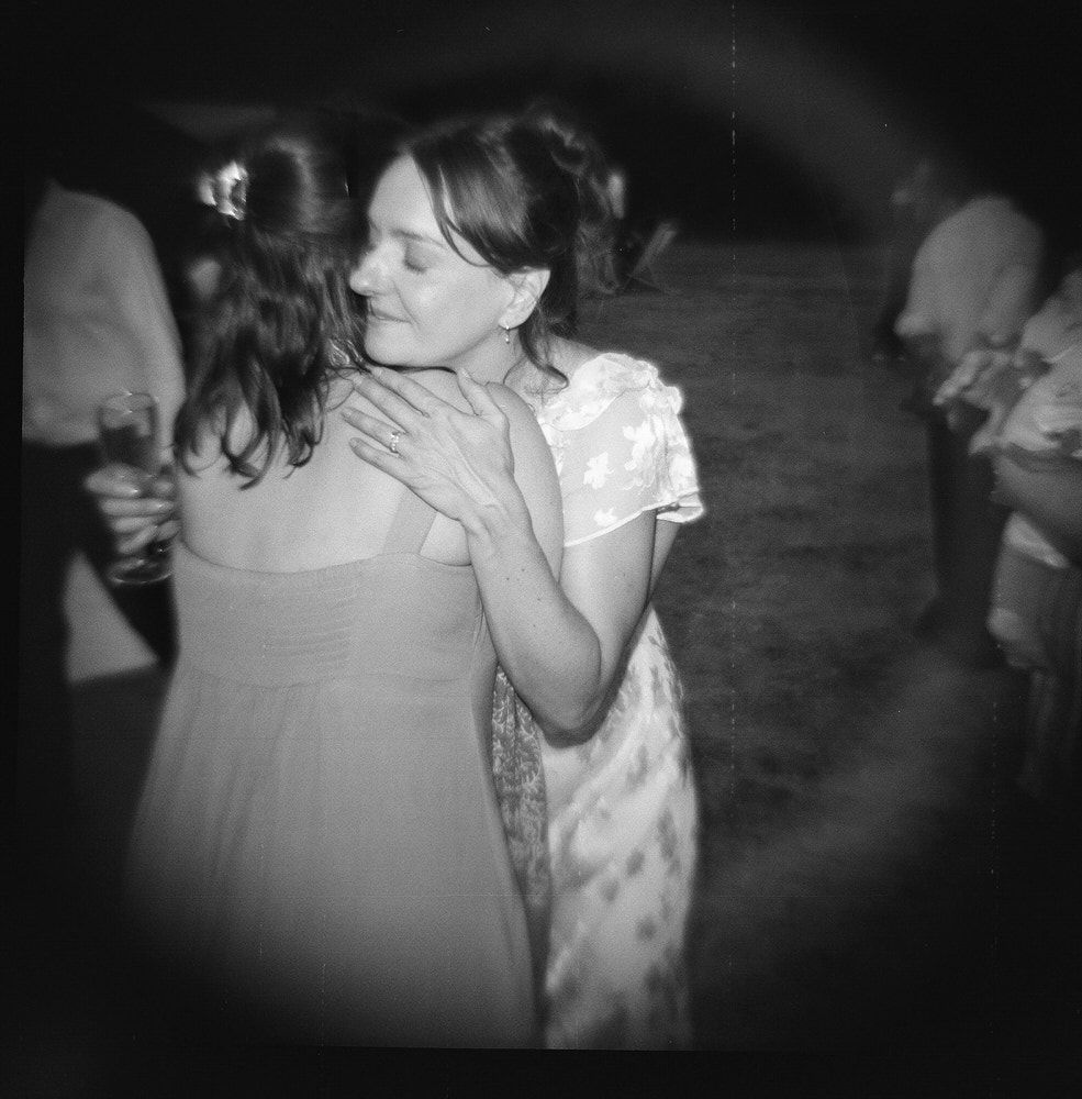 Black and white photo of two young girls hugging and dancing at an outdoor event or wedding reception.