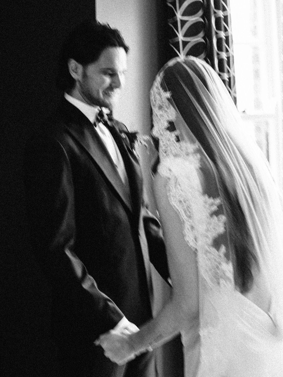 Black and white portrait of bride and groom holding hands during an intimate wedding ceremony moment.