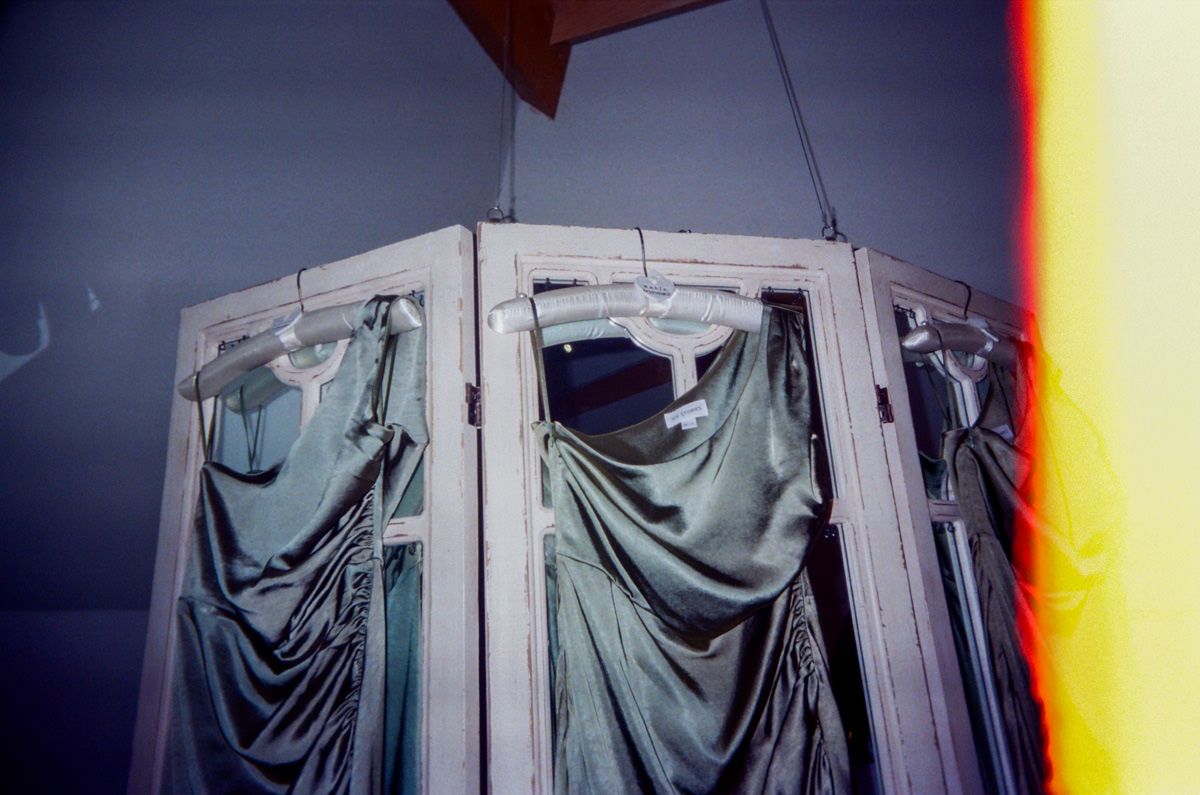 Draped fabric curtains hanging in a vintage window frame with colorful light leak effect.