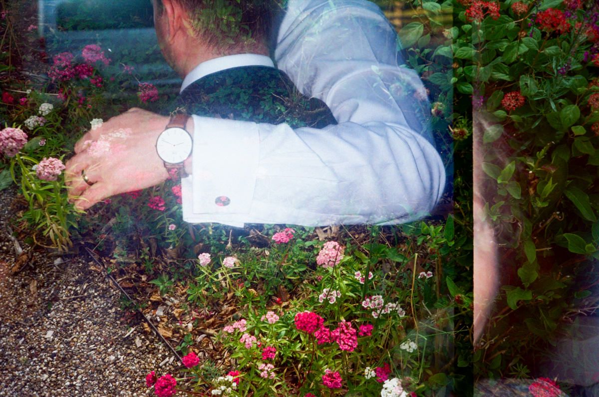 Double exposure photo of a groom wearing a watch among vibrant garden flowers at a wedding.