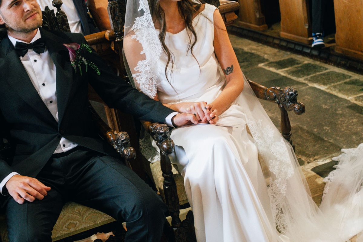 Bride and groom hold hands while seated during their church wedding ceremony.