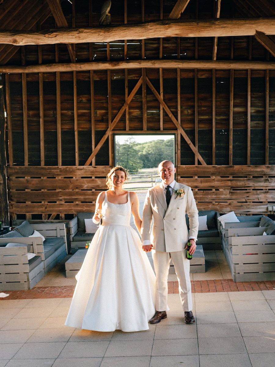Bride and groom hold hands smiling in a rustic wooden barn wedding venue.
