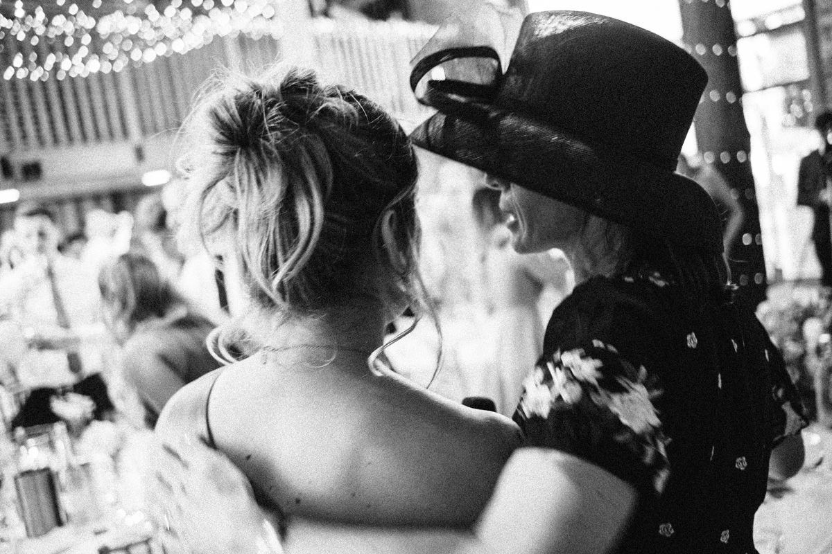 Black and white photo of two women sharing an intimate moment on a lively wedding dance floor.
