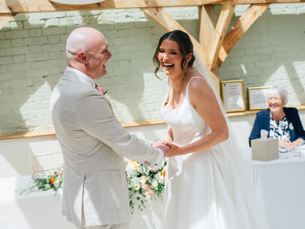 Bride and groom laughing joyfully while holding hands during wedding ceremony.