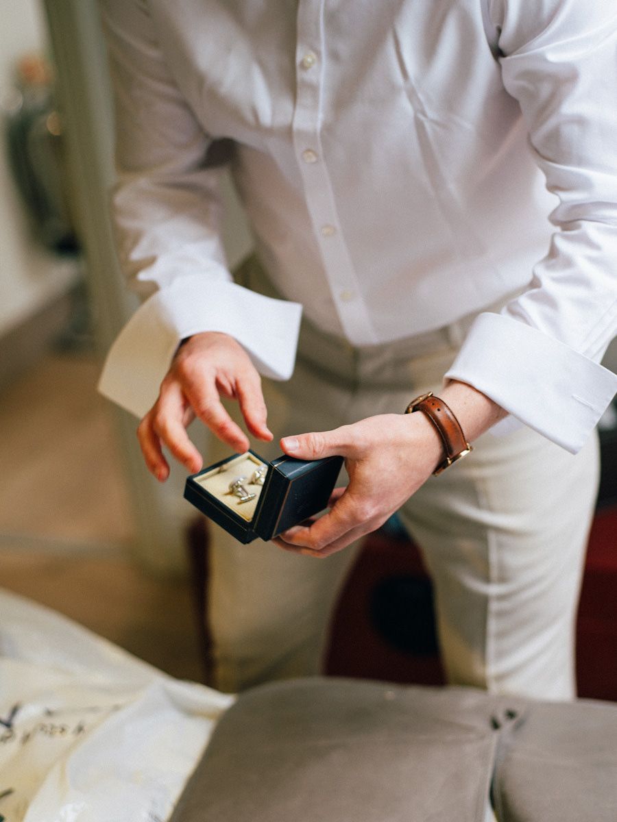 Groom in white shirt holding open a black ring box with wedding rings inside.