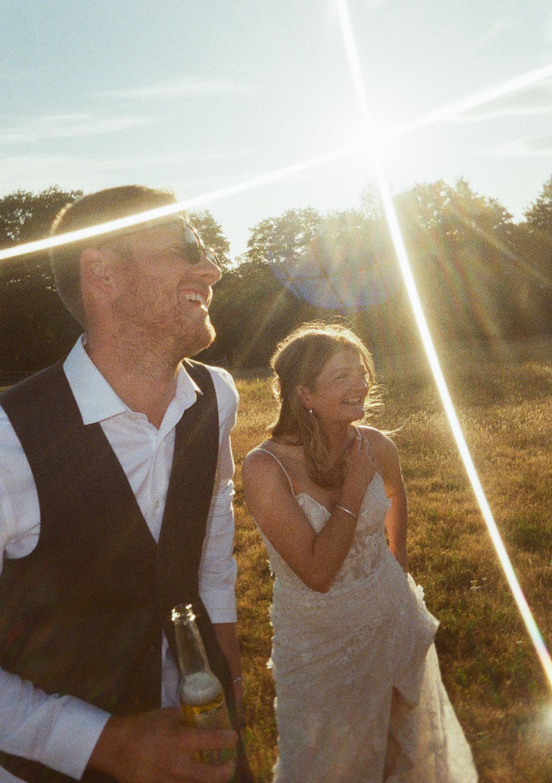 Bride and groom laughing together in golden sunlight in open field during sunset wedding portraits.
