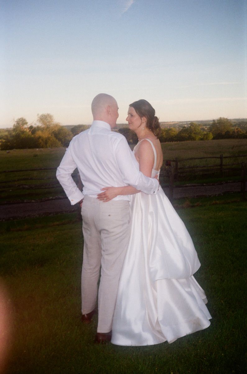 Bride and groom share a romantic moment at sunset in a lush green outdoor wedding venue.