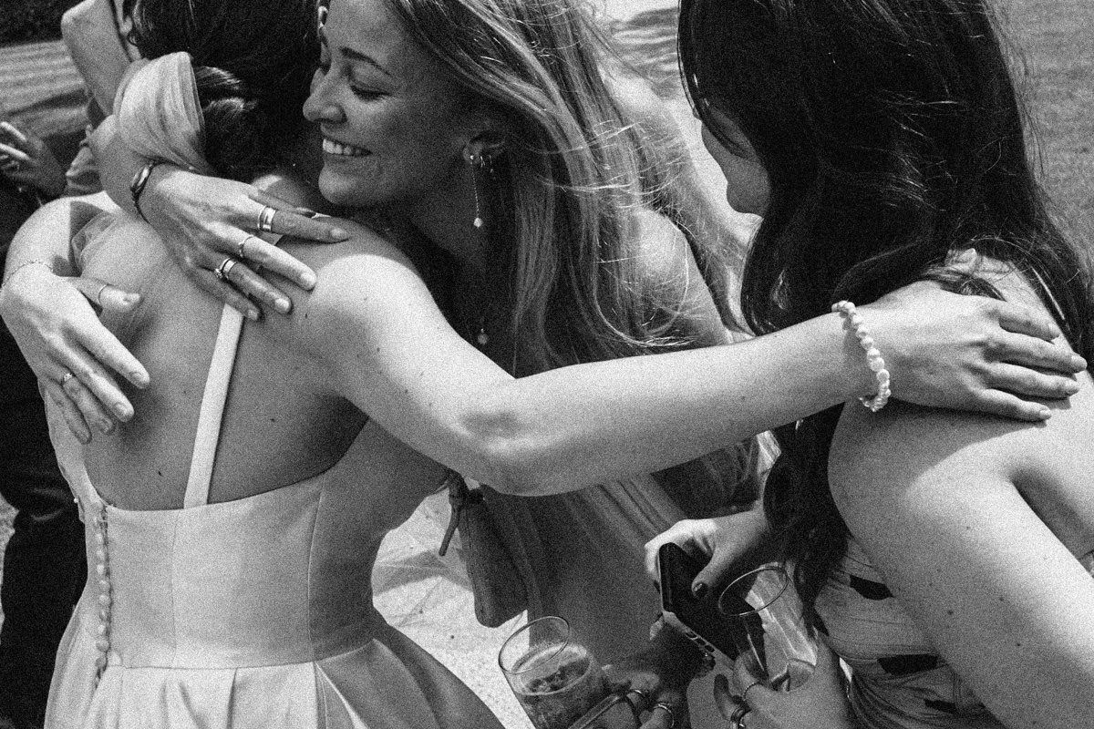 Bride receiving warm embraces from guests in emotional black and white wedding photo.