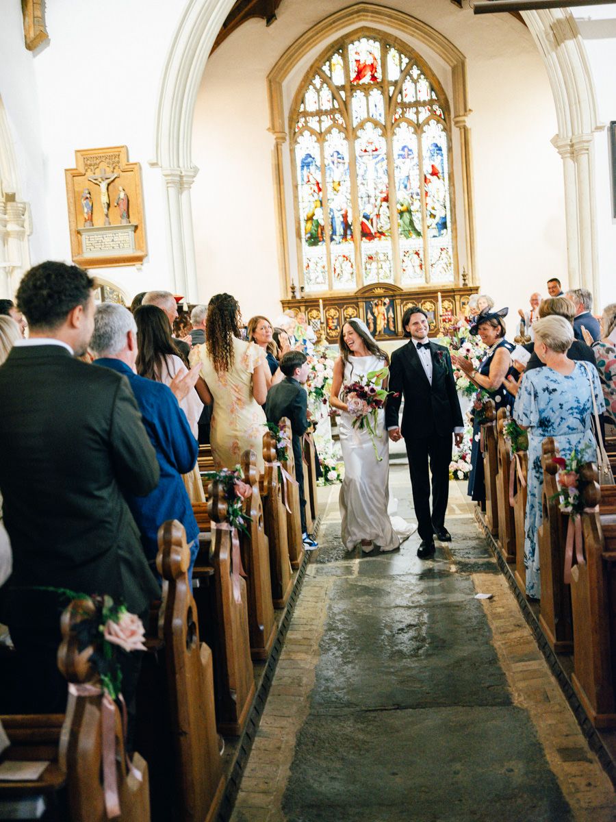 Newlyweds walk down church aisle past applauding guests after wedding ceremony.