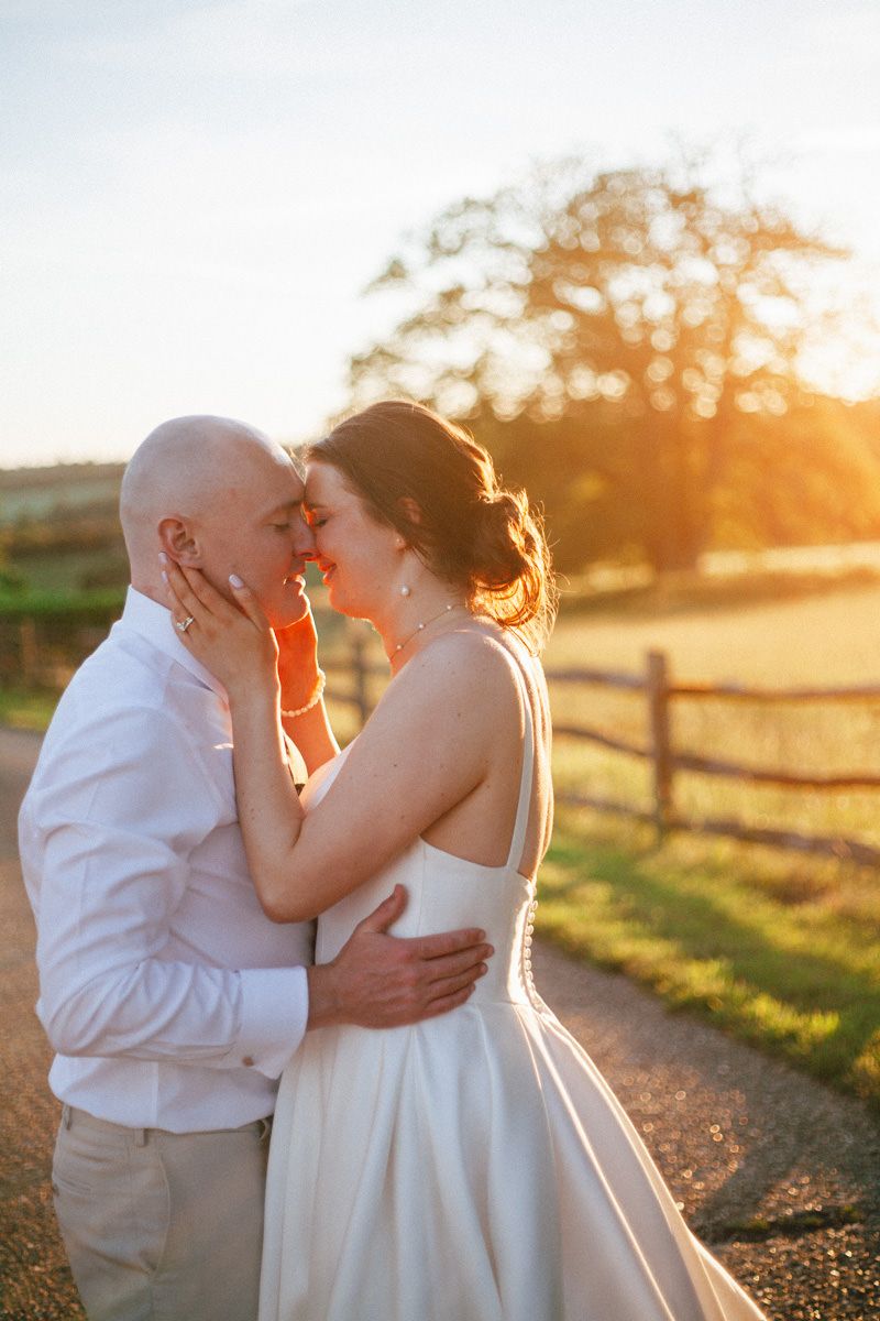 Couple shares a romantic near-kiss bathed in golden sunset light on a country lane.