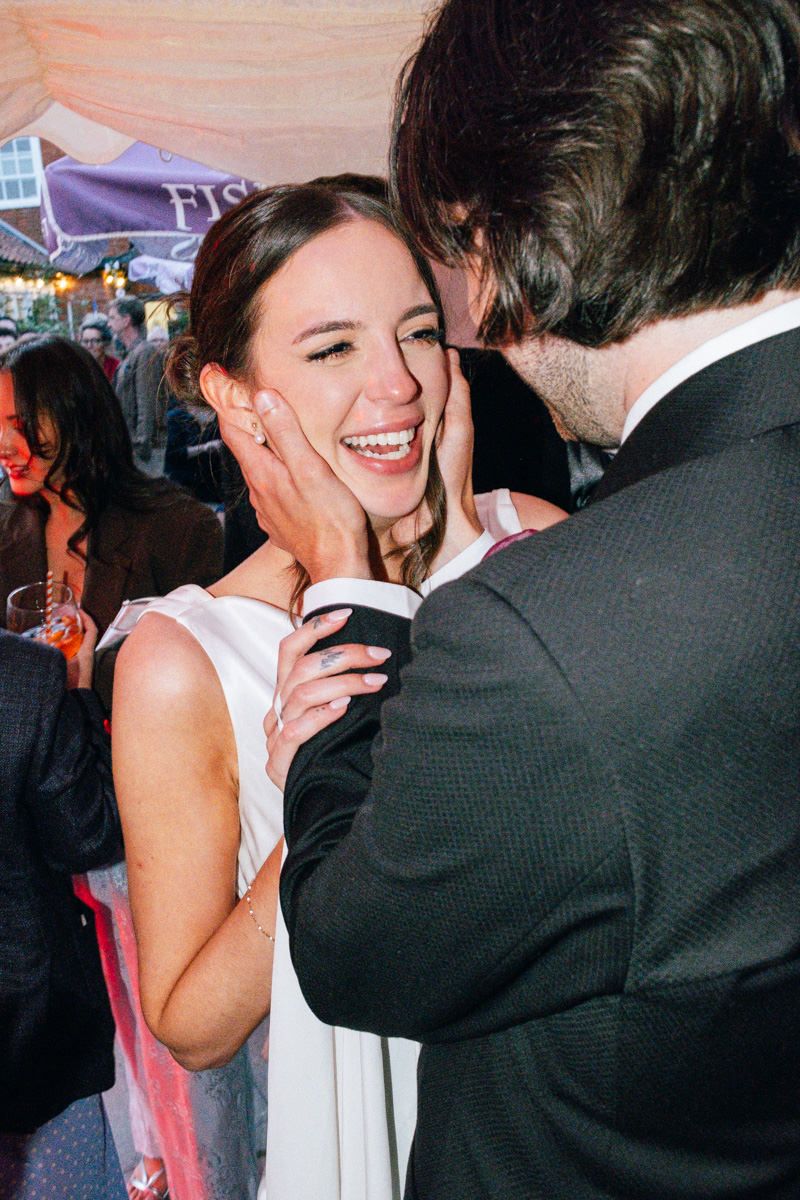 A joyful bride laughs as her groom tenderly holds her face at their wedding.