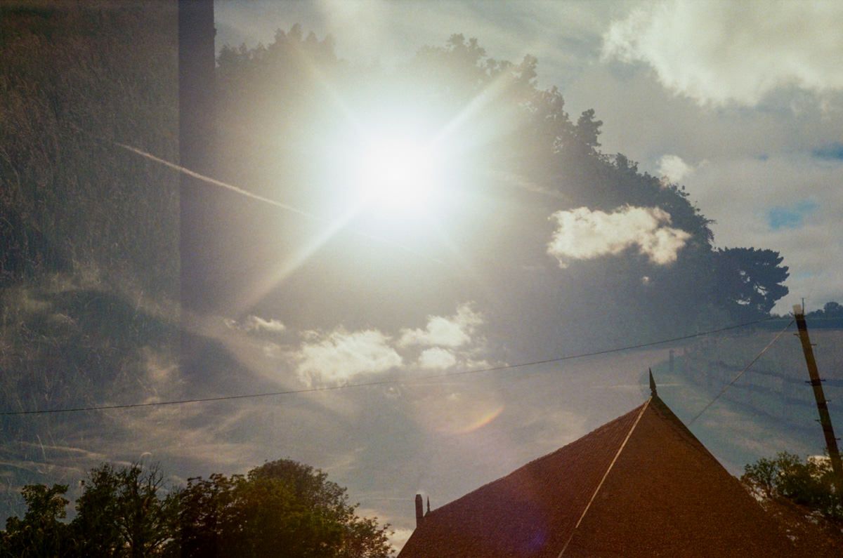 Bright sun flare over a tent rooftop with dramatic clouds and trees in the background.