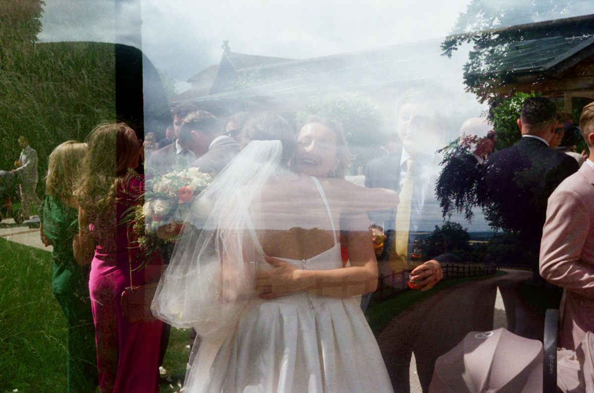 Double exposure wedding photo showing bride and groom embracing surrounded by guests outdoors.