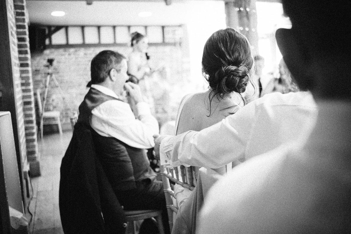 Black and white candid moment of wedding guests listening attentively during a ceremony speech.