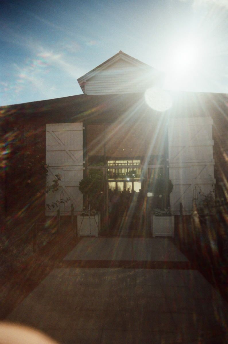 Bright sun flare over a rustic white barn wedding venue on a clear blue sky day.