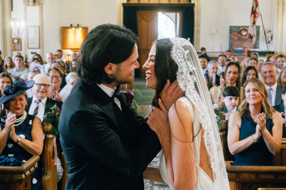 Groom tenderly holds bride's face for first kiss at church wedding altar.