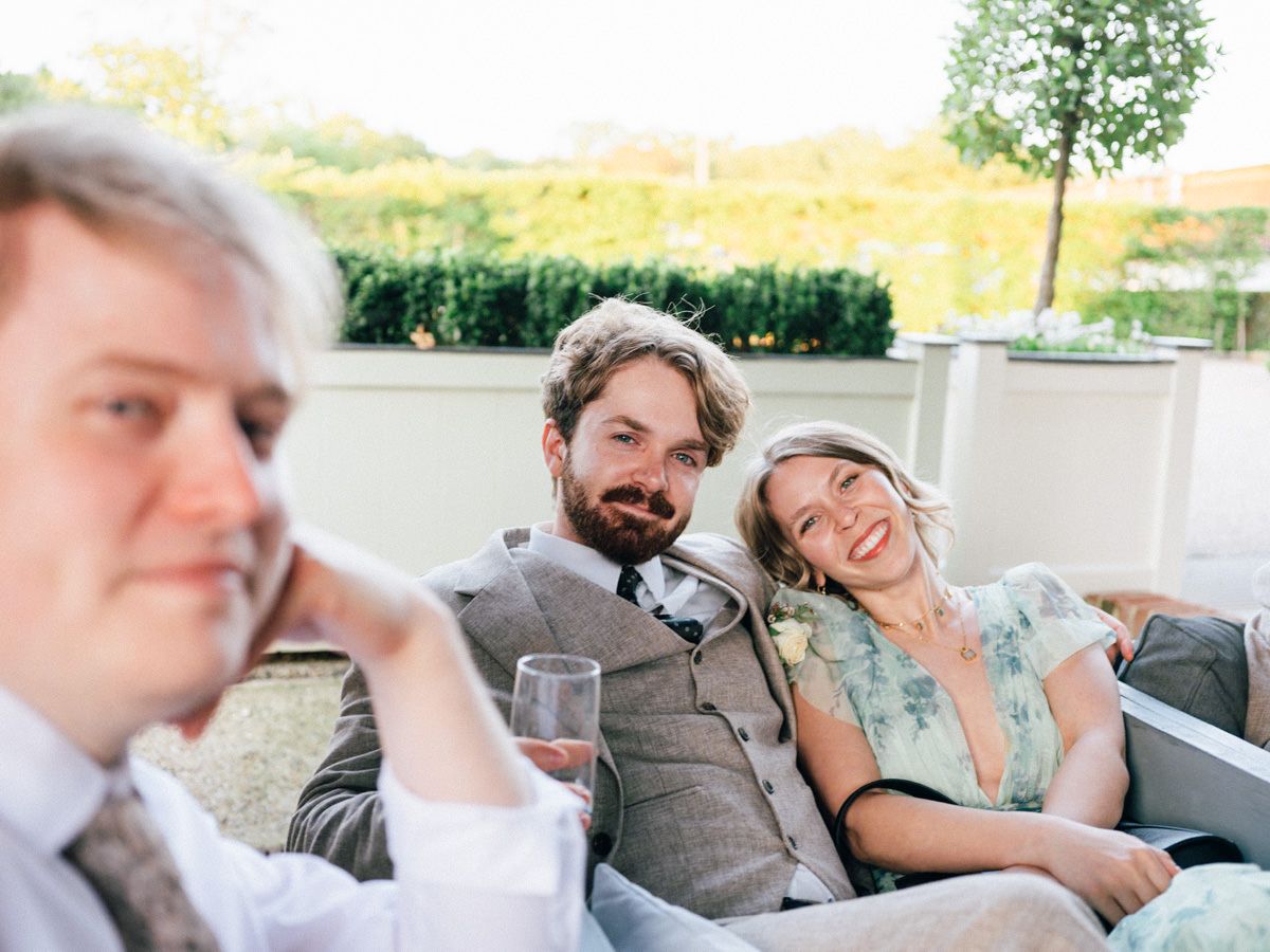 Wedding guests relaxing on outdoor sofa, smiling couple enjoying reception drinks.
