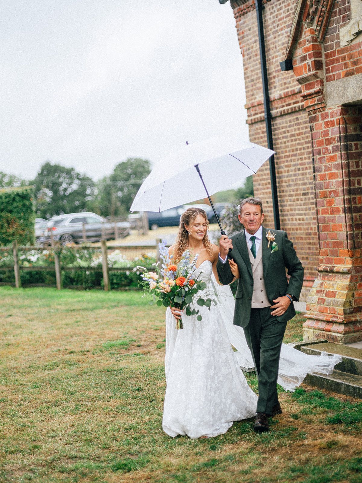 Smiling bride walking arm in arm under a white umbrella on a rainy wedding day