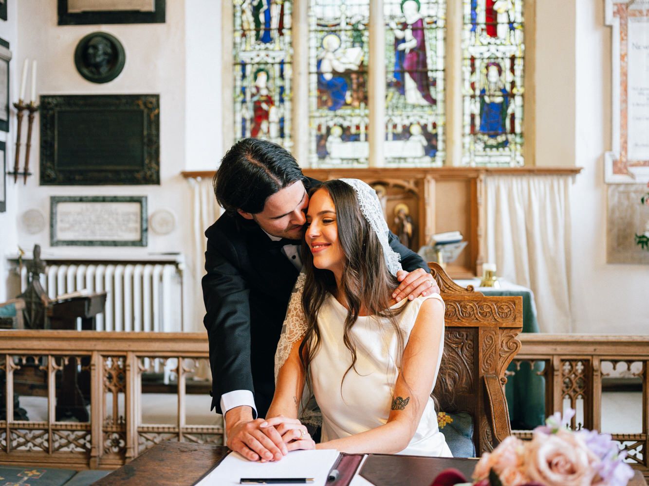 Bride and groom signing wedding register in a charming church with stained glass windows.