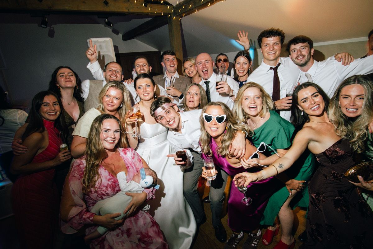 Large group of joyful wedding guests posing together at lively reception party.