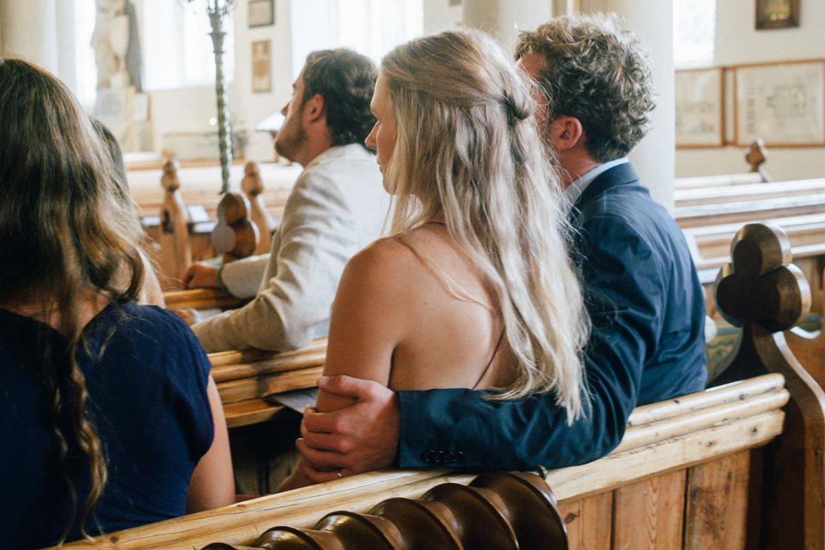 Wedding guests seated in wooden church pews during an intimate church ceremony.