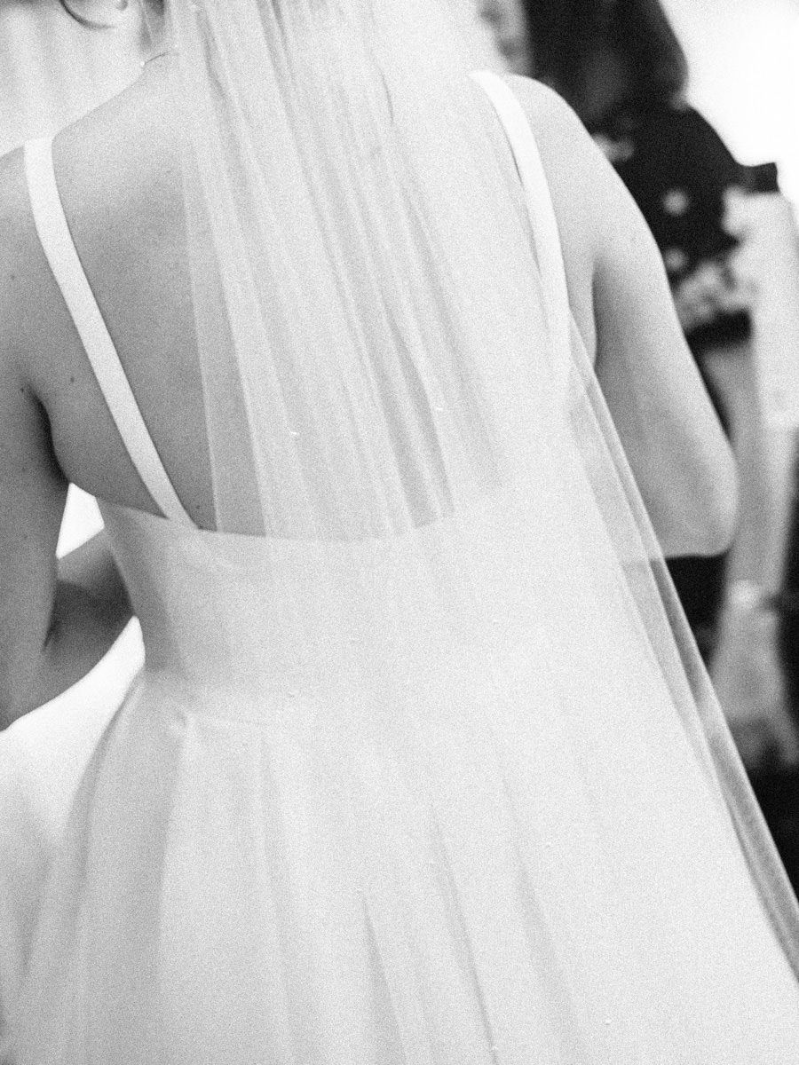 Black and white close-up of bride in backless wedding gown with flowing tulle veil.