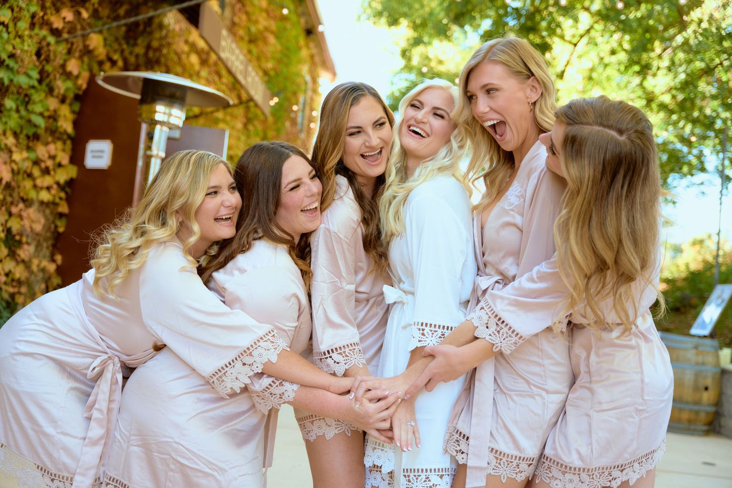 Group of bridesmaids in matching robes laughing together during pre-wedding preparations.