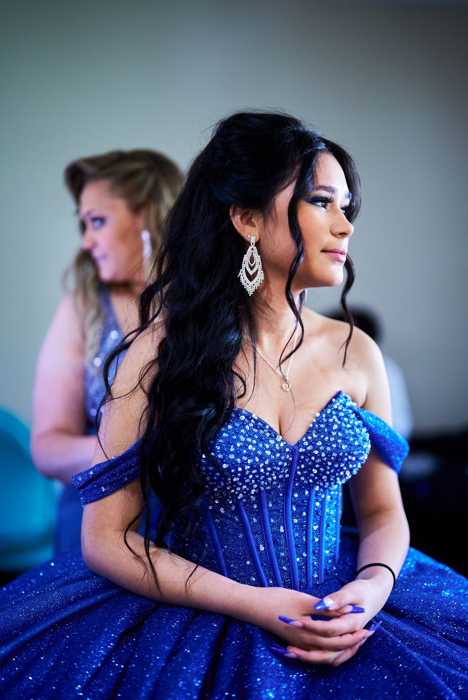 Woman in sparkling blue ball gown with off-shoulder design and long dark hair styled elegantly.