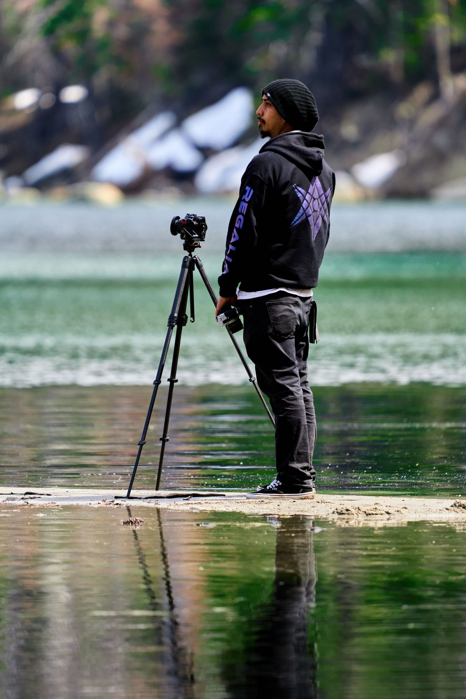 Photographer with tripod stands at water's edge capturing scenic lake views.