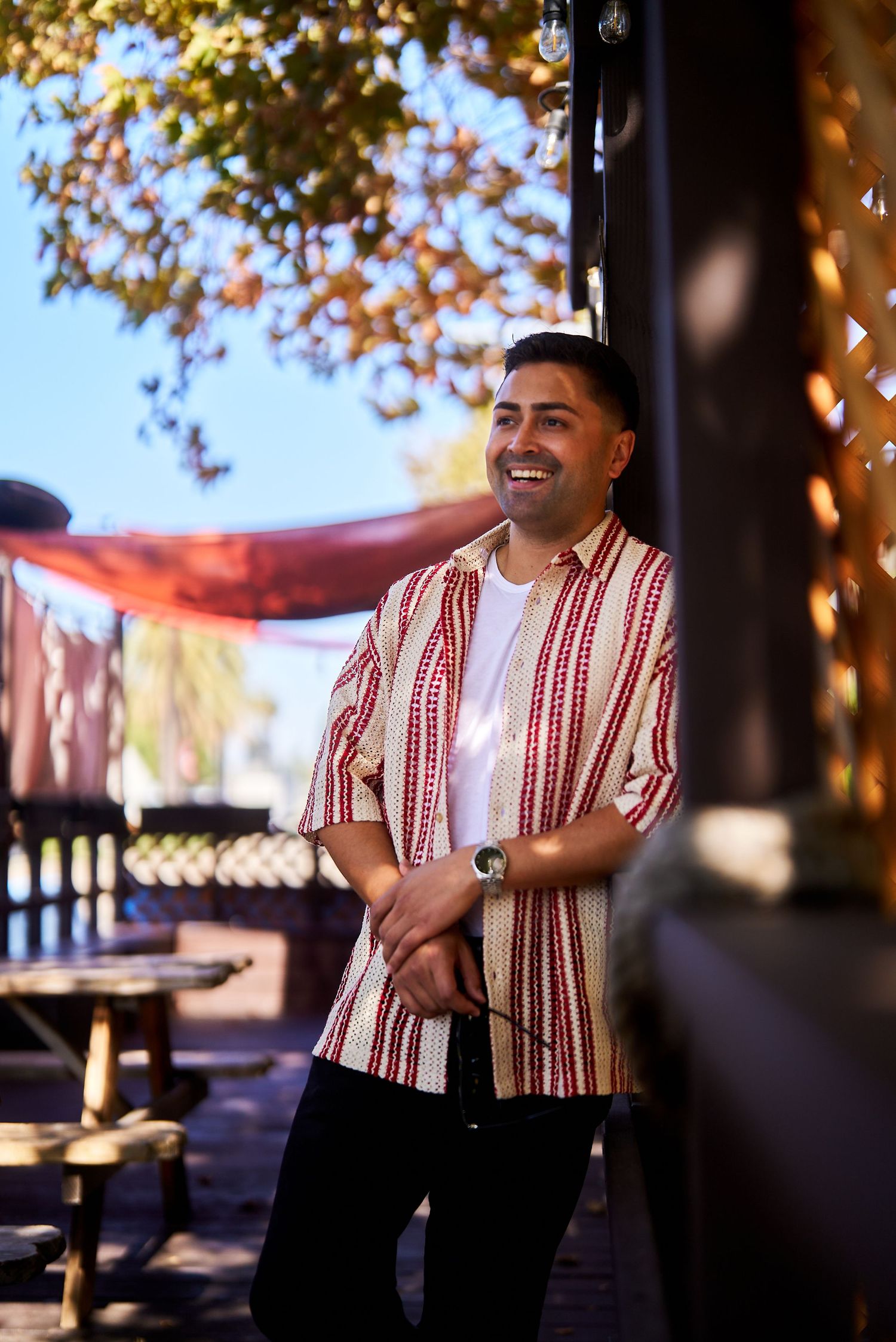 Person in a striped shirt smiling while standing on a patio with autumn decorations.